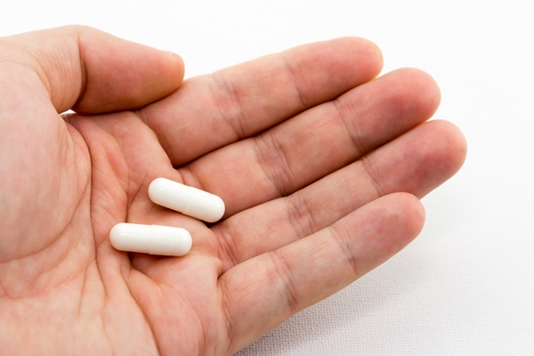 A closeup shot of a person holding two white capsules with a white background